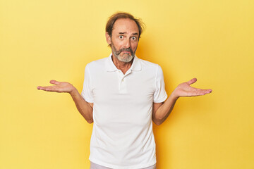 Caucasian middle-aged man in yellow studio doubting and shrugging shoulders in questioning gesture.