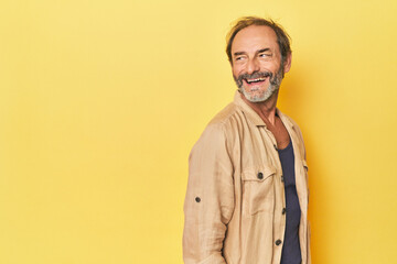 Obraz premium Caucasian middle-aged man in yellow studio looks aside smiling, cheerful and pleasant.