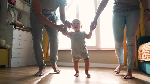 First steps. Family day. toddler takes first steps at home across field. parents hold hands of baby learn to walk. Happy baby takes first steps on floor of house.toddler dream to learn the first steps