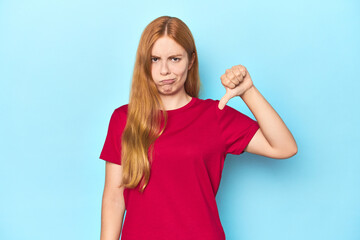 Fototapeta premium Redhead young woman on blue background showing thumb down, disappointment concept.