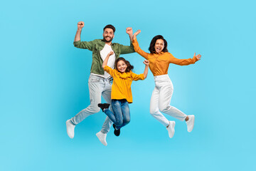 Overjoyed family of three jumping gesturing yes and smiling, parents and daughter posing together...