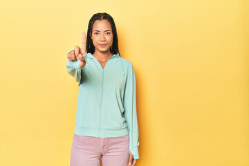 Indonesian sporty woman on yellow backdrop showing number one with finger.