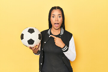 Indonesian schoolgirl with soccer ball on yellow pointing to the side