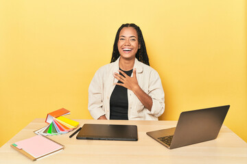 Indonesian designer with tools at table on yellow showing a dislike gesture, thumbs down....