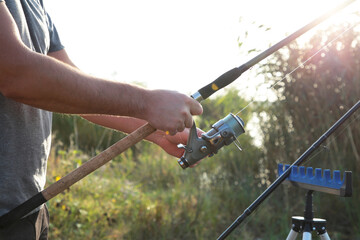 Man holding a fishing rod standing on a bridge over a river in the village where he is a regular outdoor fishing on a fun and relaxing holiday.