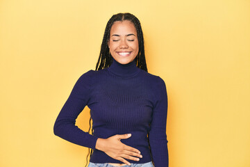 Young Indonesian woman on yellow studio backdrop touches tummy, smiles gently, eating and...