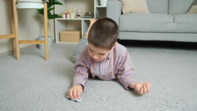 A little boy plays with a toy car lying on the floor alone.