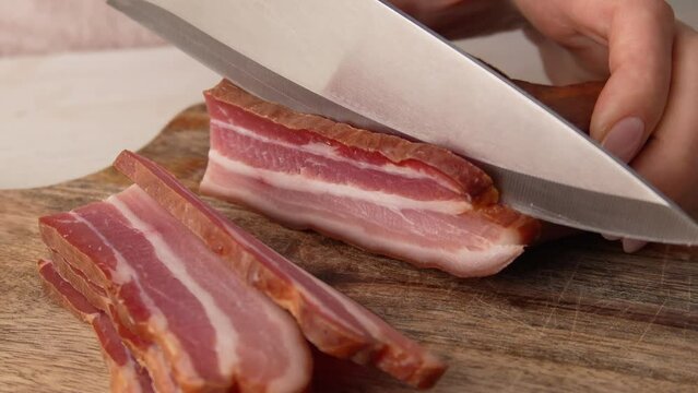 Making pasta carbonara - Slicing pancetta bacon into pieces on a wooden cutting board with a knife. Dried smoked meat. Traditional food.