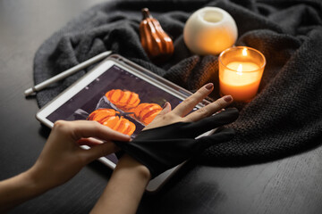 Girl puts on  special glove to draw still life picture with pumpkins on electronic tablet near burning candle. The concept of inspiration, creativity, modern art. Halloween, Thanksgiving day