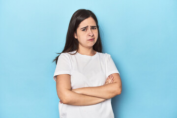 Young Caucasian woman on blue backdrop suspicious, uncertain, examining you.