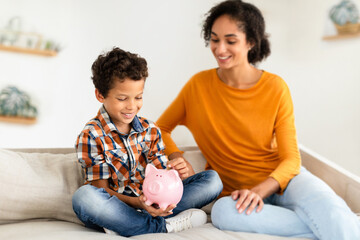 Fototapeta premium Happy Boy And Mom Holding Piggybank, Putting Coin At Home