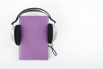 Audiobook on white background. Headphones put book, empty cover, copy space for ad text. Distance...