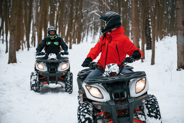 Fototapeta na wymiar Man is looking behind at his friend. Two people are riding ATV in the winter forest