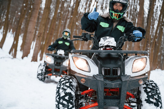 Woman with her friend. Two people are riding ATV in the winter forest