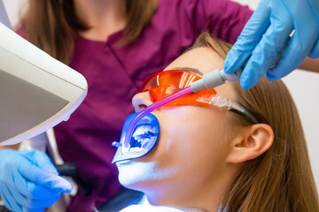 A dentist utilizing a saliva ejector during the teeth whitening treatment for a young patient.