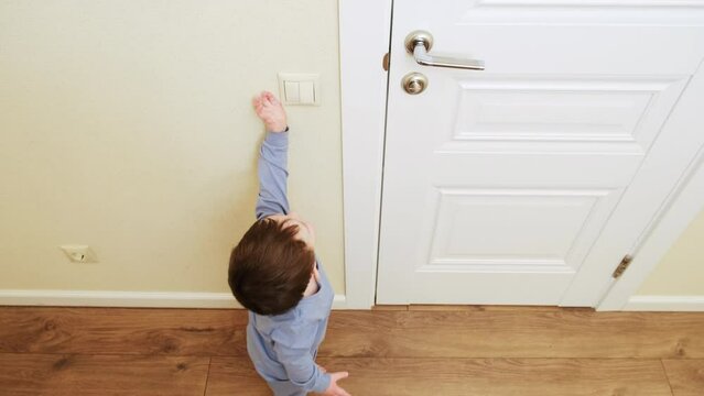 Little baby turns on the light by pressing the switch. Small child turns off the electric light at the white door. Kid about two years old (age one year nine months)