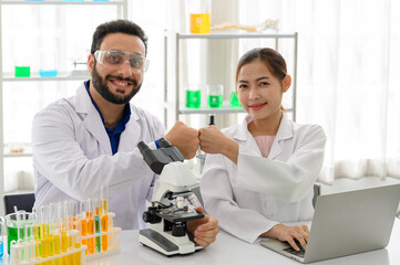 Man and woman scientists smiling confident bump fists at laboratory