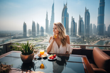 Beautiful young woman having breakfast on a terrasse of a luxury hotel, overlooking the skyscrapers in Dubai