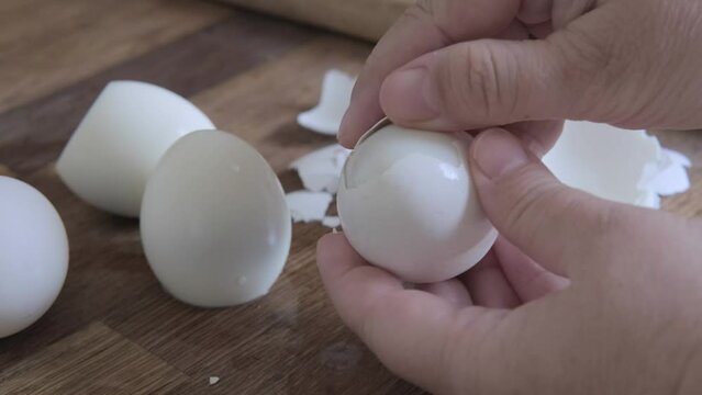 closeup of female hands peel white boiled eggs from shell, chicken eggs on wooden table, valuable food product, Easter culinary traditions, cooking at home, protein meals