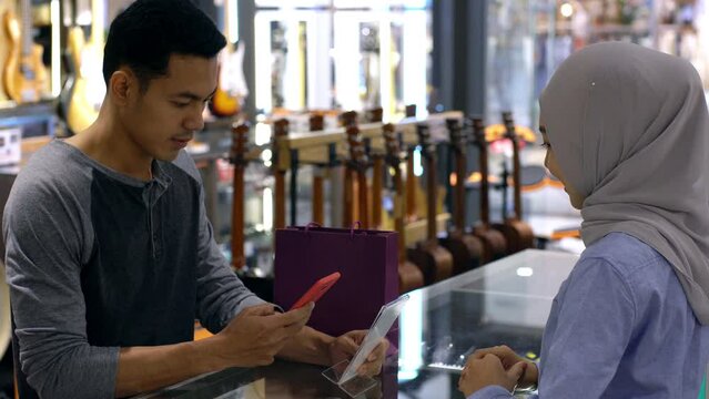 An upwardly mobile Asian Muslim man using a mobile phone to pay for a product at a sale terminal with QR code, nfc identification payment for verification and authentication