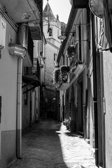 Grayscale of a narrow street with traditional Italian buildings on a sunny summer day in Lauria