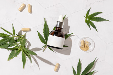 Dropper bottle with CBD cosmetic and capsules near cannabis leaves top view, hard shadows