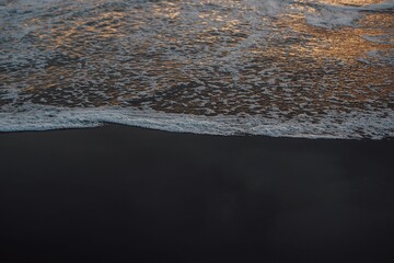 Black sand beach, ocean waves crashing on black sand beach during golden hour