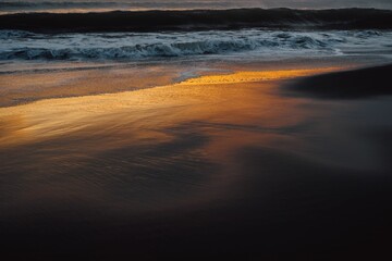 Black sand beach, ocean waves crashing on black sand beach during golden hour