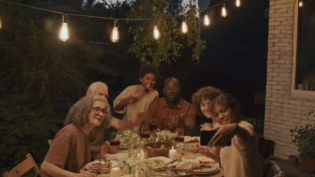 Black girl holding smartphone taking photos with her family during celebration dinner in summer evening