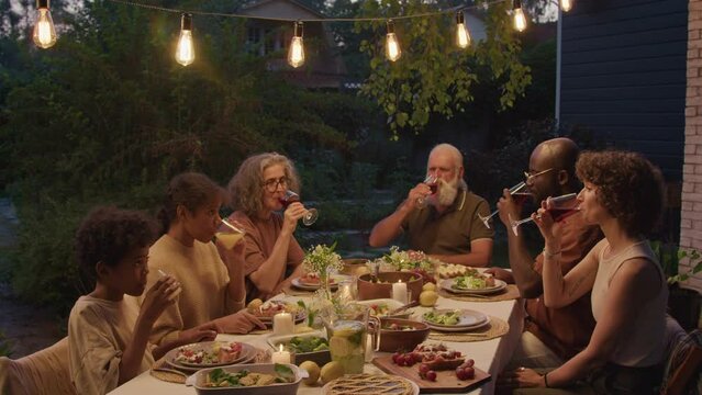 Ethnically Diverse Family Wearing Casual Clothes Having Celebration Dinner Outdoors On Summer Evening