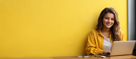 Smiling teen girl using laptop for online study on yellow background Happy student in educational webinar - obrazy, fototapety, plakaty