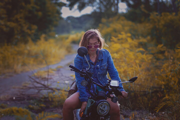 beautiful woman wearing blue jeans jacket sitting on enduro motorcycle against colorful natural  background