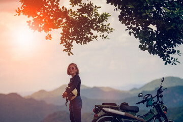 woman holding safety helmet standing beside enduro motorcycle against beautiful mountain scene of khaoyai national park thailand