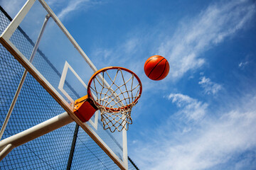 Street basketball ball falling into the hoop against blue cloudy sky. Success, scoring, winning and achieving the goal concept © Yelena