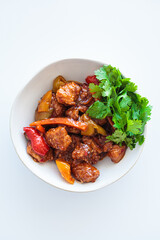 Stewed chicken fillet pieces with vegetables in white bowl with cilantro.