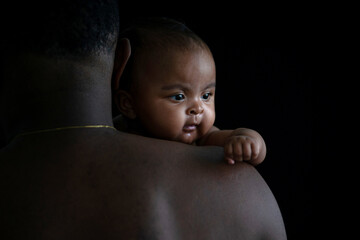 Portrait of shirtless African father holding baby girl on black background