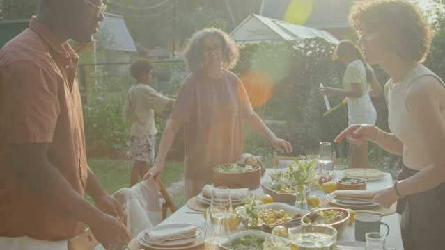 African American and Caucasian men and women setting table for meal in backyard on sunny summer day