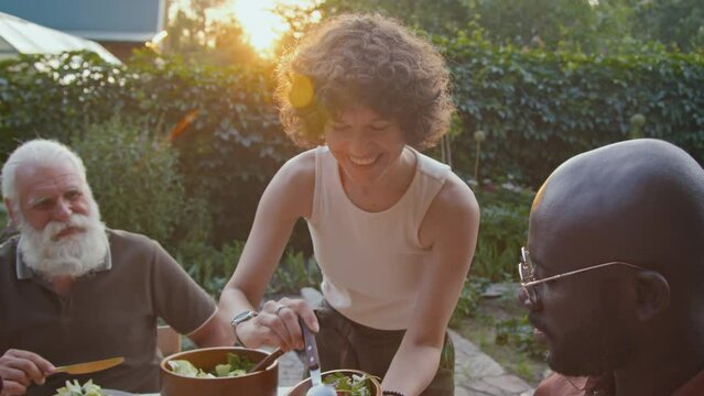 Caucasian woman dishing out fresh salad during family dinner on summer evening in backyard