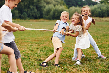 Playing tug of war game. Kids are having fun on the field at daytime together