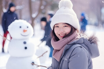 Young asian chinese woman building snowman at the park in winter