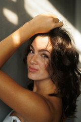 Naklejka premium Beautiful brunette woman in white top and blue jeans. Girl smile, happy. Portrait of young pretty woman. Complicated sunlight with shadows. White background. Light from window, portrait.