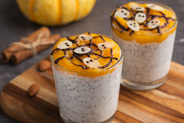 Chia seed pudding with pumpkin puree in glasses on dark background. A table decorated with pumpkins. Fall time. Healthy breakfast. Homemade dessert.