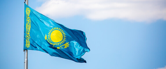 The flag of Kazakhstan is fluttering in the wind against the blue sky. The flag is located on the blue dome of the administrative building. The city of Astana is the administrative center.