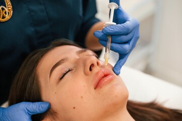 Naklejka premium Cosmetologist does injection for lips augmentation. Women's cosmetology in the beauty salon