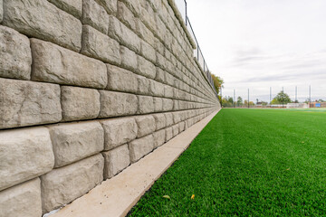 Retaining wall next to a green synthetic turf athletic field.