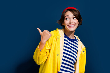 Photo of young model girl wear red beanie hat yellow raincoat striped sweater point finger carhartt brand isolated on blue color background