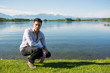 A young attractive man kneeling down next to a body of water. Photo of a man kneeling by the...
