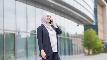 Pregnant business woman in hijab and suit talking on smartphone. 