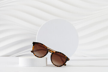 Woman's Tortoiseshell frame sunglasses on a podium on a white background. Trendy sunglasses still...