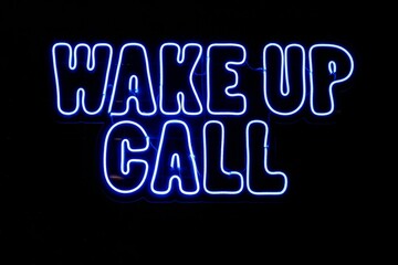 Bright neon sign of 'Wake Up Call' illuminated in the darkness against a black background